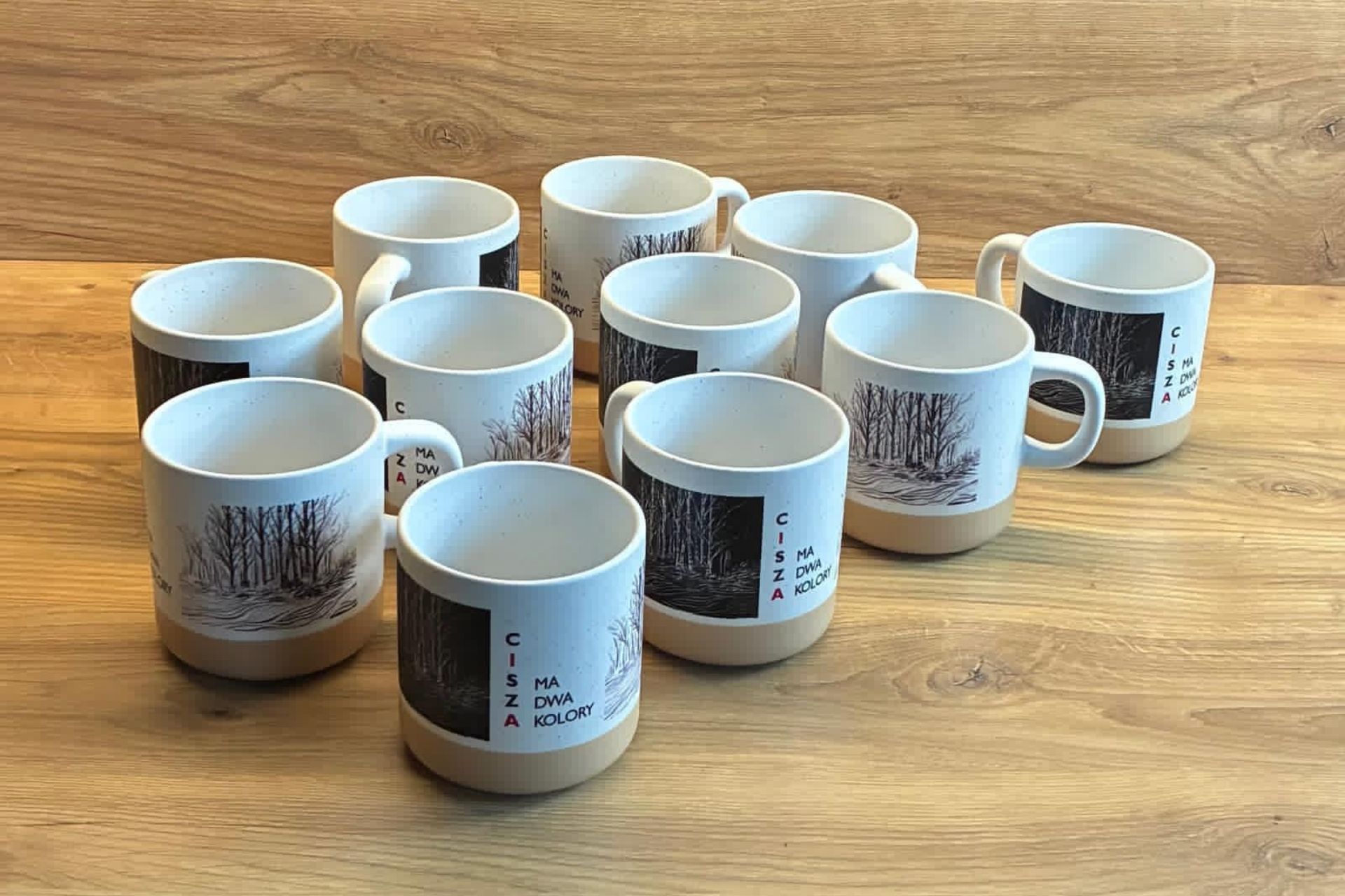 Ceramiczne kubki z grafiką brzóz i z cytatem „Cisza ma dwa kolory”.